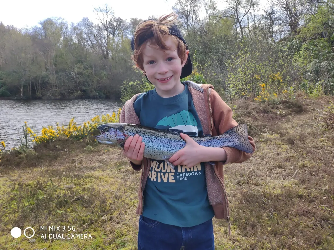 A young angler holding a fish beside the lake